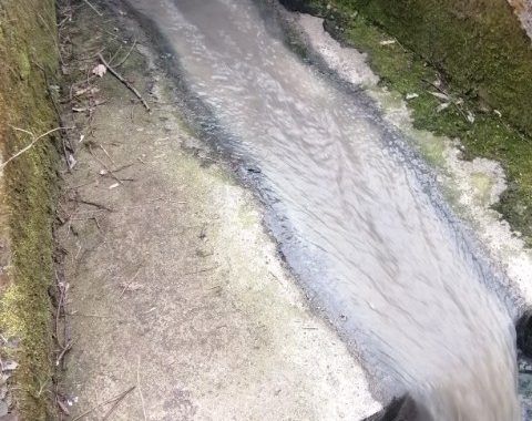 Zrzut ścieków koloru szarego do rzeki z betonowego odpływu